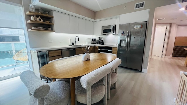 kitchen with light wood-type flooring, tasteful backsplash, stainless steel appliances, sink, and white cabinetry