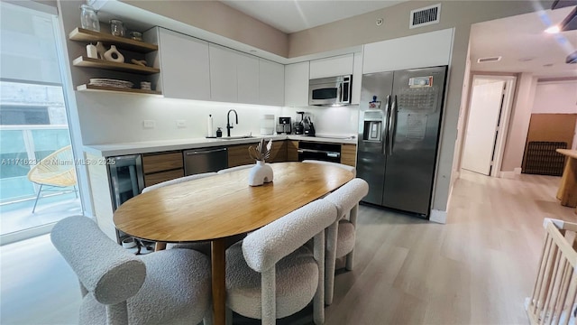 kitchen featuring sink, beverage cooler, light hardwood / wood-style floors, white cabinets, and black appliances