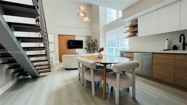 dining area with sink, a towering ceiling, and light hardwood / wood-style floors