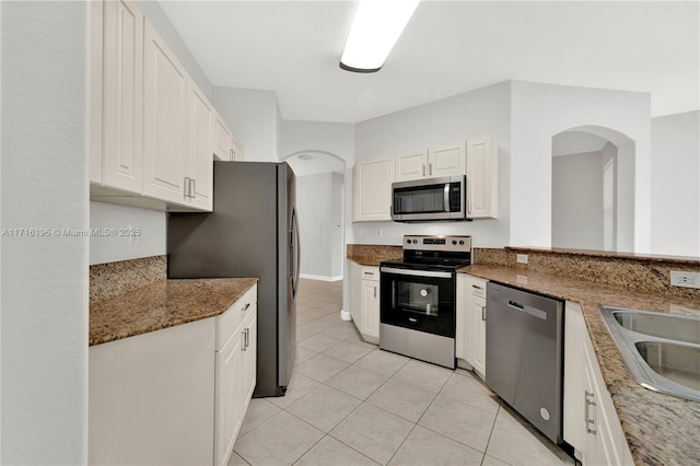 kitchen with appliances with stainless steel finishes, stone countertops, a sink, and white cabinetry