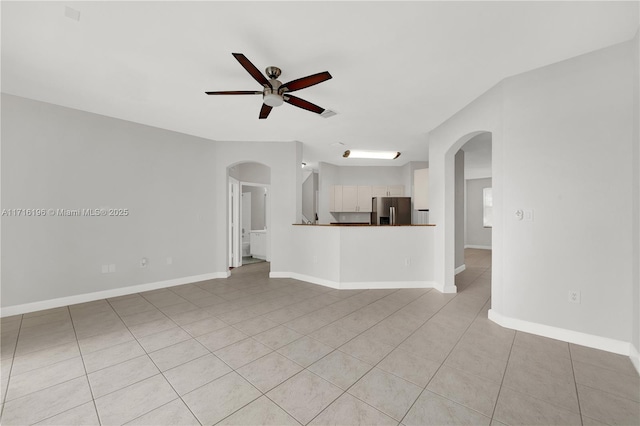 unfurnished living room featuring arched walkways, ceiling fan, light tile patterned floors, and baseboards