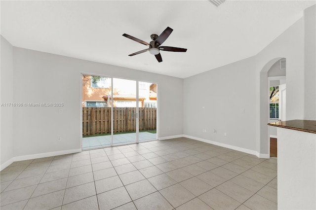 spare room featuring light tile patterned floors, ceiling fan, baseboards, and arched walkways