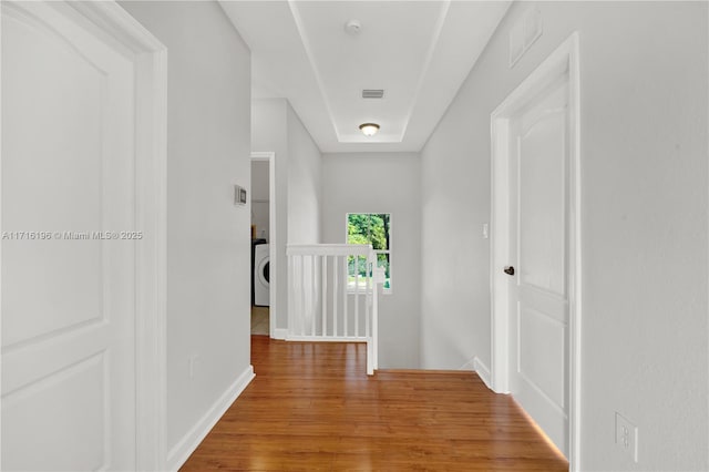 corridor featuring attic access, an upstairs landing, wood finished floors, washer / dryer, and baseboards