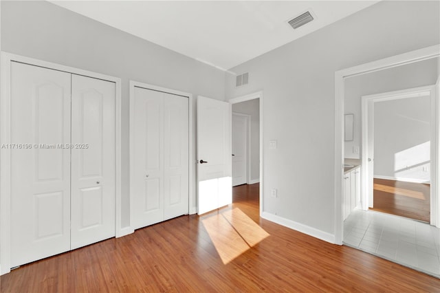 unfurnished bedroom featuring multiple closets, light wood-type flooring, visible vents, and baseboards