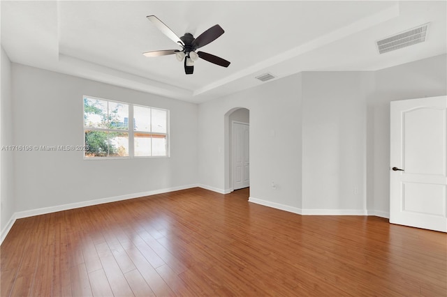 empty room featuring dark wood-style floors, arched walkways, a raised ceiling, and visible vents