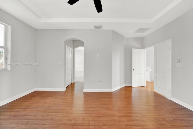 unfurnished room featuring arched walkways, visible vents, baseboards, light wood-type flooring, and a tray ceiling