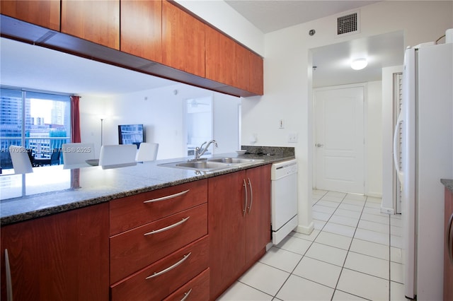 kitchen featuring dark stone countertops, white appliances, sink, and light tile patterned floors