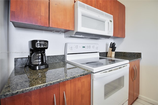 kitchen with tile patterned flooring, white appliances, and dark stone counters