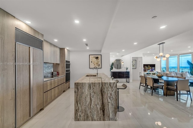 kitchen with a center island with sink, a sink, decorative light fixtures, and modern cabinets