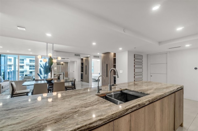 kitchen featuring light stone counters, a sink, open floor plan, modern cabinets, and pendant lighting