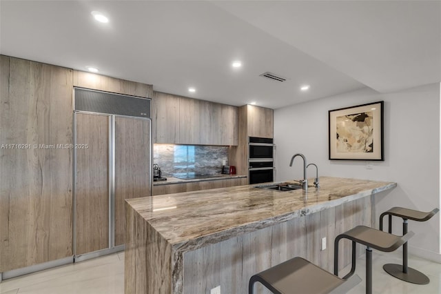 kitchen with light stone counters, a breakfast bar, double wall oven, a sink, and paneled fridge