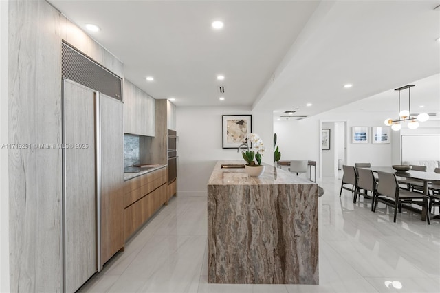 kitchen with light stone countertops, pendant lighting, a center island with sink, and paneled built in fridge