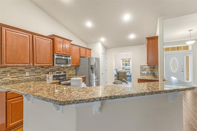 kitchen featuring kitchen peninsula, a kitchen bar, stainless steel appliances, stone countertops, and lofted ceiling