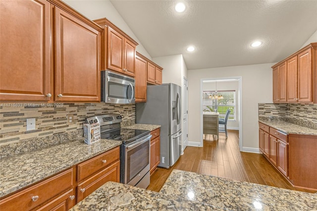 kitchen with lofted ceiling, light hardwood / wood-style flooring, light stone counters, stainless steel appliances, and a chandelier