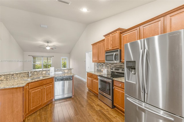 kitchen featuring decorative backsplash, appliances with stainless steel finishes, light stone counters, vaulted ceiling, and sink