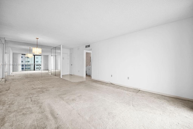 empty room with a textured ceiling, light colored carpet, and an inviting chandelier