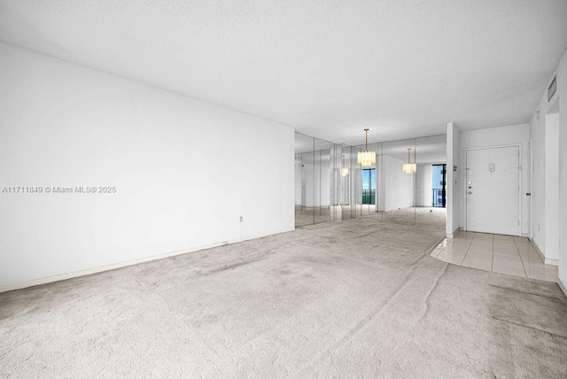 spare room with a chandelier, a textured ceiling, and light colored carpet