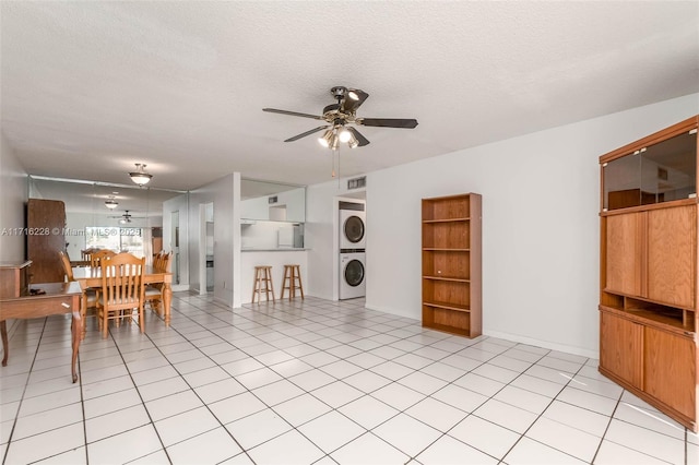 interior space with light tile patterned floors, a textured ceiling, ceiling fan, and stacked washer and clothes dryer