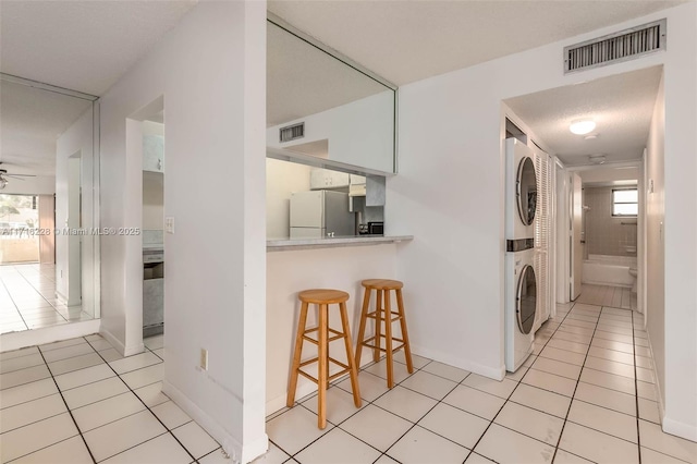 laundry area featuring light tile patterned floors, a textured ceiling, stacked washing maching and dryer, and ceiling fan