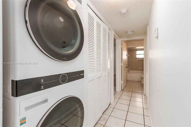 washroom with stacked washer / drying machine, light tile patterned floors, and a textured ceiling