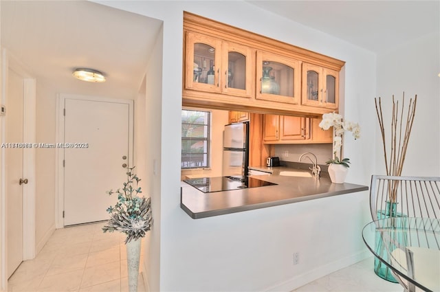 kitchen featuring light brown cabinets, sink, light tile patterned floors, black electric cooktop, and stainless steel refrigerator