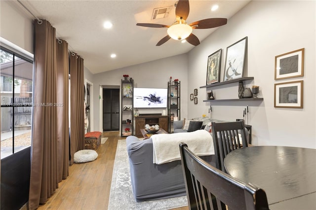 living room featuring a textured ceiling, light hardwood / wood-style flooring, vaulted ceiling, and ceiling fan