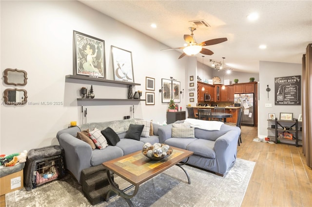 living room with a textured ceiling, light hardwood / wood-style floors, ceiling fan, and lofted ceiling