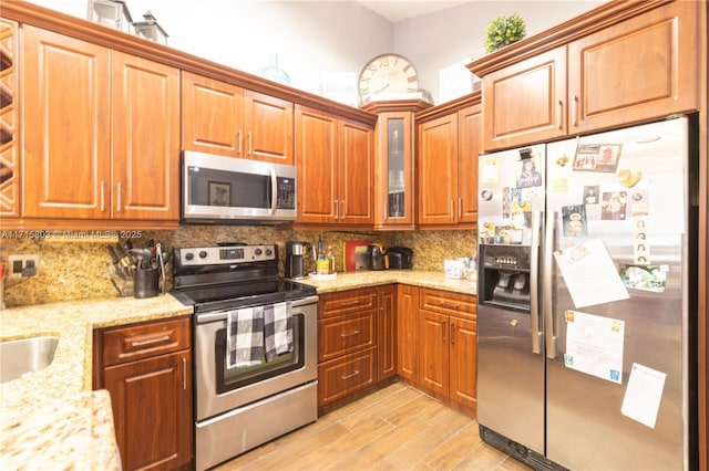 151 NW 115th Ave Unit 405, Plantation, FL 33325 - kitchen featuring appliances with stainless steel finishes, backsplash, light stone countertops, glass insert cabinets, and brown cabinets