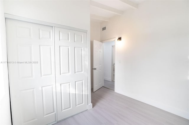 unfurnished bedroom with beamed ceiling, light hardwood / wood-style floors, and a closet