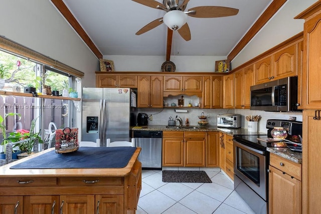 kitchen with sink, stainless steel appliances, tasteful backsplash, dark stone counters, and light tile patterned floors