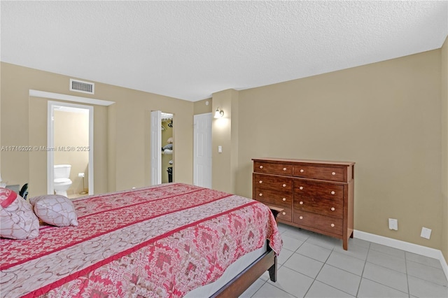 bedroom with ensuite bath, light tile patterned floors, and a textured ceiling