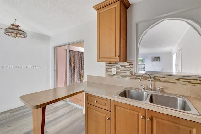 kitchen with kitchen peninsula, tasteful backsplash, a textured ceiling, sink, and light hardwood / wood-style floors