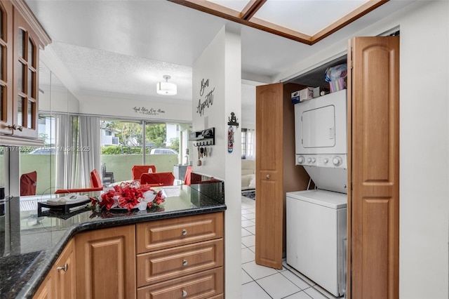 laundry area featuring stacked washer and dryer, light tile patterned floors, and a textured ceiling