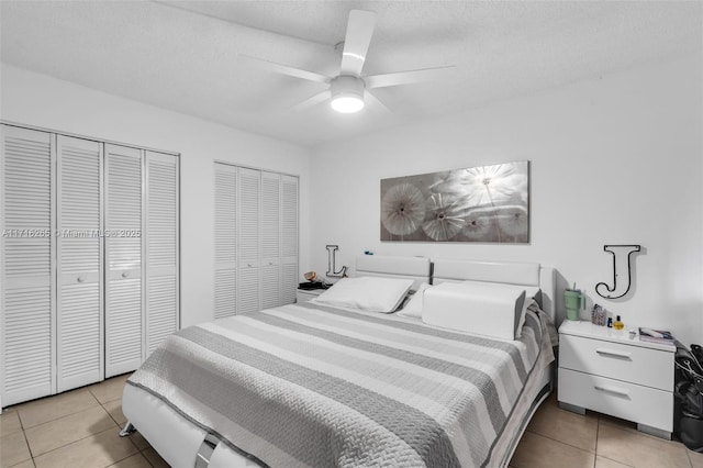 bedroom with light tile patterned floors, a textured ceiling, two closets, and ceiling fan