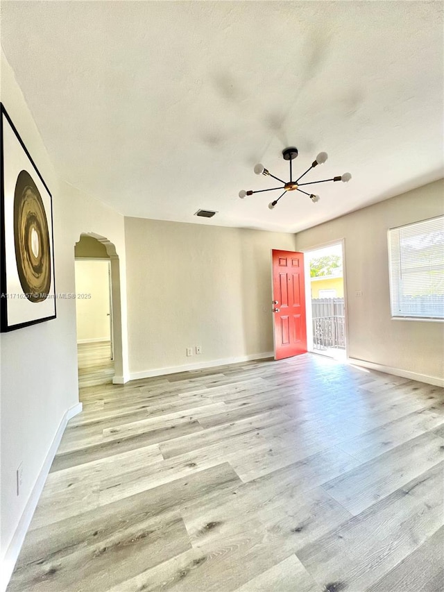 empty room with a notable chandelier, a textured ceiling, and light hardwood / wood-style flooring