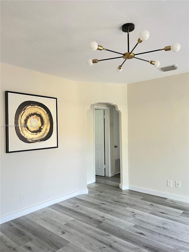 spare room featuring light wood-type flooring and a chandelier