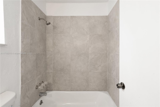 bathroom with toilet and tiled shower / bath