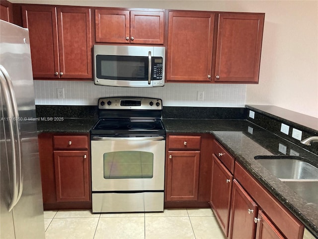 kitchen featuring light tile patterned floors, sink, stainless steel appliances, and dark stone countertops