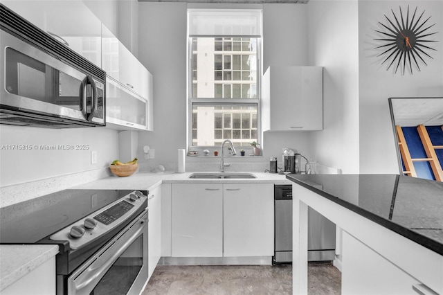 kitchen with appliances with stainless steel finishes, white cabinetry, dark stone counters, and sink