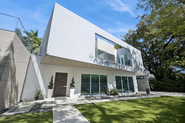 rear view of property with a balcony, stucco siding, and a lawn