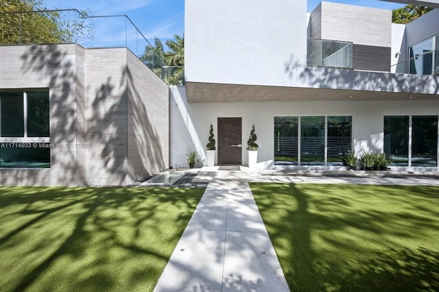 rear view of property featuring a lawn and stucco siding