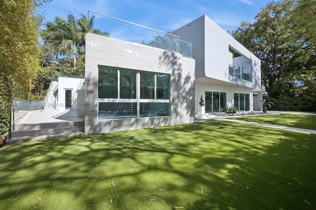 back of property featuring a lawn, a balcony, and stucco siding