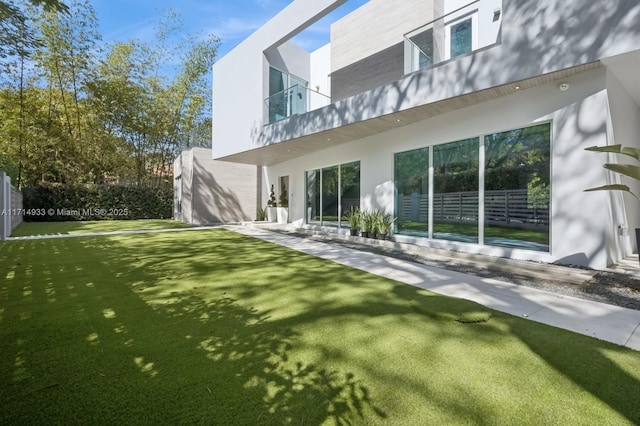 rear view of house with a lawn, stucco siding, and fence