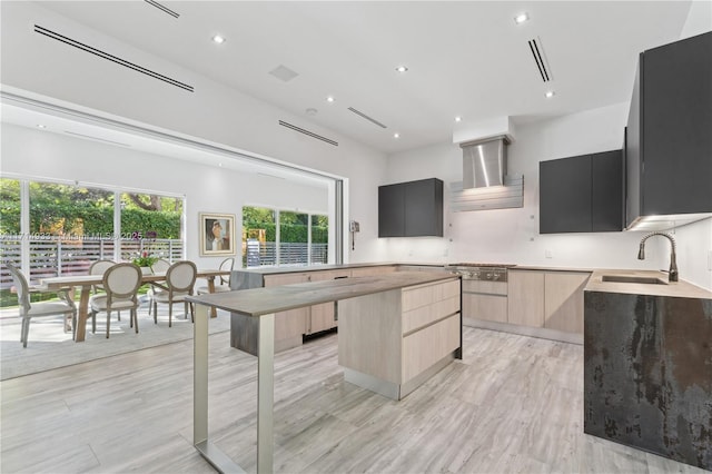 kitchen with a sink, wall chimney exhaust hood, light brown cabinetry, modern cabinets, and a center island