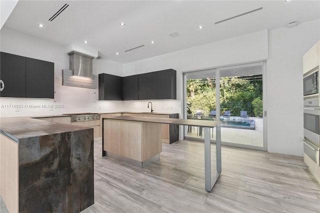 kitchen featuring modern cabinets, stainless steel appliances, wall chimney exhaust hood, dark cabinetry, and a center island