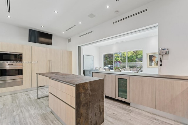 kitchen featuring a warming drawer, stainless steel oven, light brown cabinetry, beverage cooler, and modern cabinets