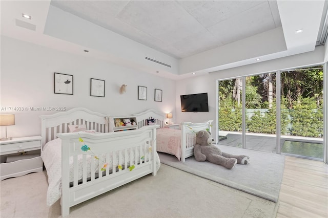 bedroom with a tray ceiling, wood finished floors, and access to outside