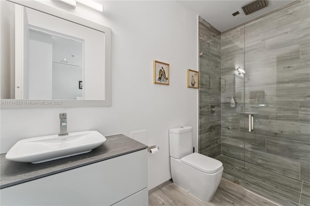 bathroom with toilet, vanity, a shower stall, wood finished floors, and visible vents