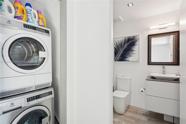 clothes washing area featuring laundry area, a sink, stacked washing maching and dryer, and wood finished floors