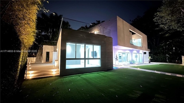 back of house at night featuring a lawn and stucco siding